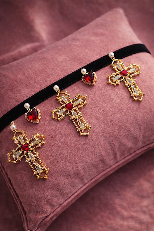 Cross My Heart Jeweled Charm Bridal Choker flat lay with black velvet ribbon, ornate gold cross charms, red jeweled heart charms, and pearls on a blush velvet pillow