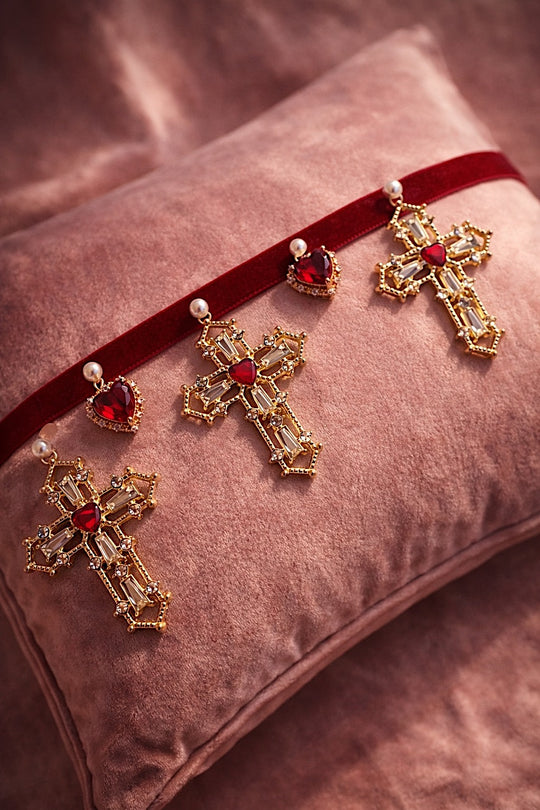 Cross My Heart Jeweled Charm Bridal Choker flat lay with deep red velvet ribbon, ornate gold cross charms, red jeweled heart charms, and pearls on a blush velvet pillow