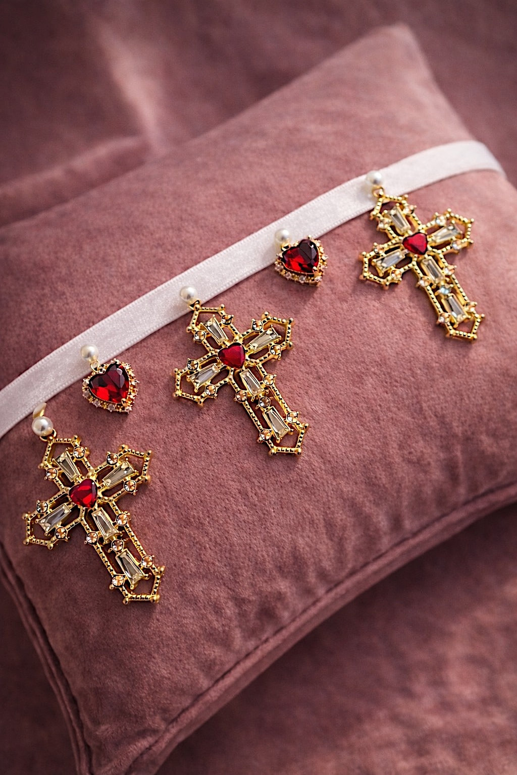 Cross My Heart Jeweled Charm Bridal Choker flat lay with white ribbon, ornate gold cross charms, red jeweled heart charms, and pearls on a blush velvet pillow
