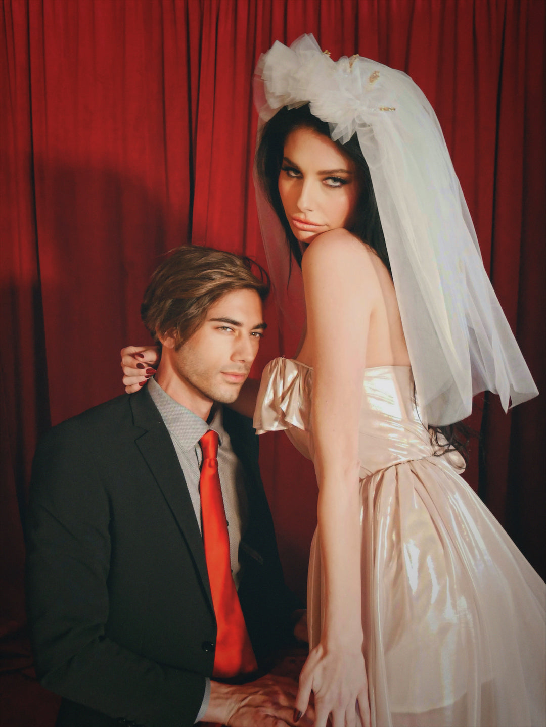 Portrait of brunette bride wearing the Cross My Heart Jeweled Charm Wedding Veil beside a man in a black suit and red tie