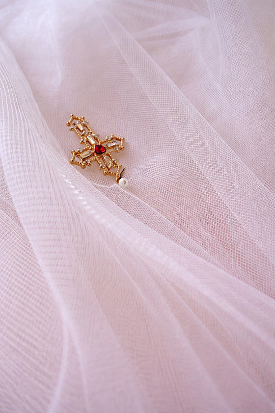 Detail of the Cross My Heart Jeweled Charm Wedding Veil comb with pearls, jeweled hearts, and ornate gold cross charms on soft ivory tulle