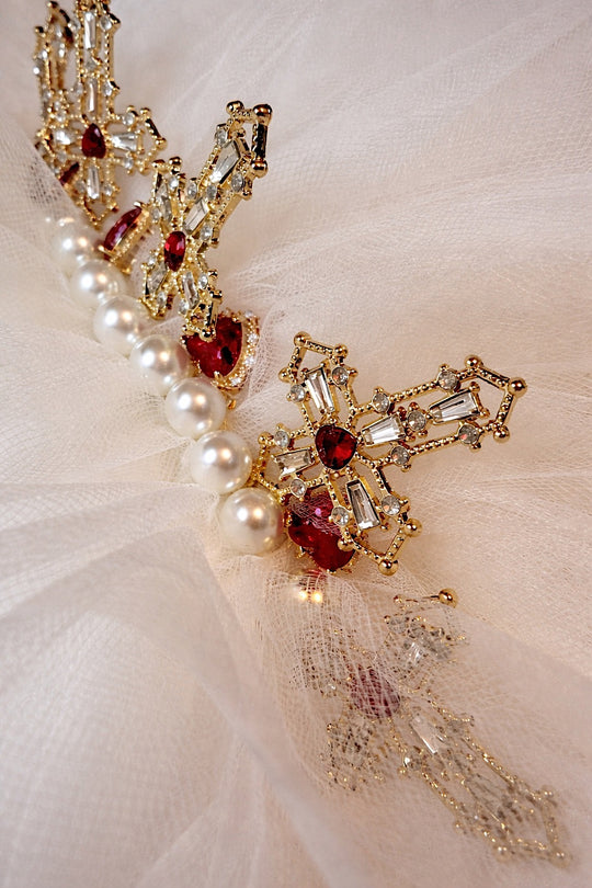 Close-up of ornate gold cross charms, pearls, and red jeweled heart details on the Cross My Heart Jeweled Charm Wedding Veil