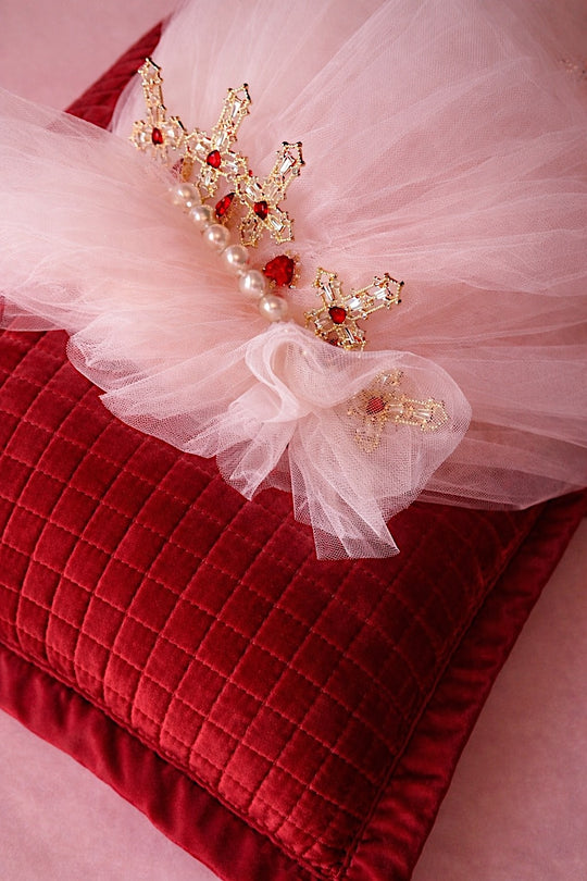Detail of the Cross My Heart Jeweled Charm Wedding Veil comb with pearls, ivory tulle, and gold cross charms on a red velvet pillow