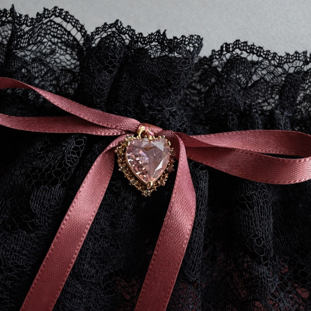 Close detail of crystal heart charm on black lace bridal garter with satin bow