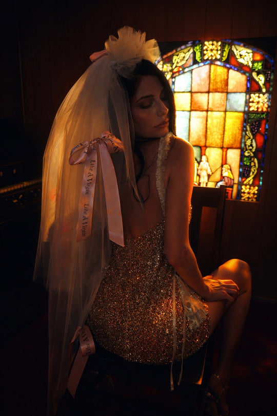 Editorial bridal portrait wearing Like A Virgin satin bow wedding veil with blush printed ribbons and soft tulle layers