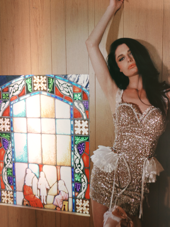 A brunette bride in sparkly mini wedding dress posing beside stained glass window.